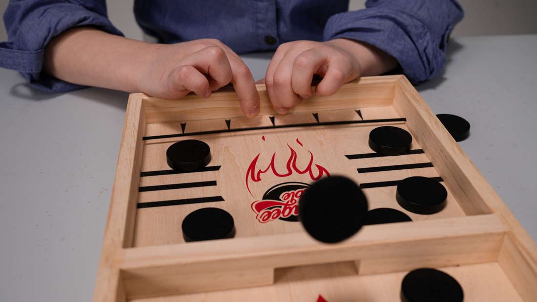 A child's hands are seeing as they play the sling puck game Bungee table. One puck is flying off the board and is on focus, adding dynamic to the image.